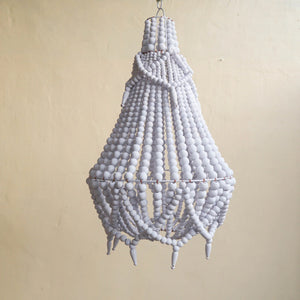 Handmade white beaded chandelier with a tiered boho design against a neutral wall.