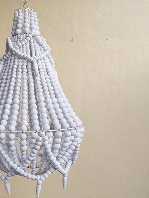Handmade white beaded chandelier with natural boho decor style against a beige wall.
