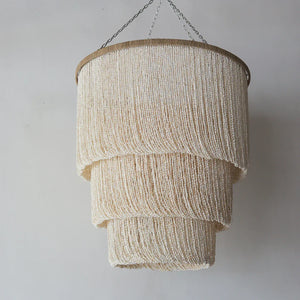 Handmade Balinese seashell chandelier with tiered beaded design against a light wall.