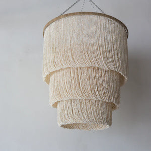 Handmade tiered seashell chandelier with natural finish, hanging against a plain wall
