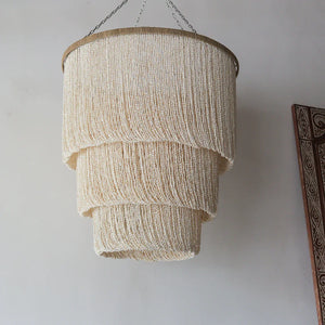 Handmade cream seashell chandelier with tiered design, hanging in a minimalist room