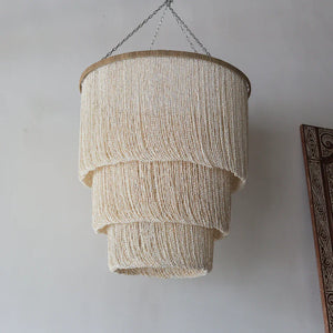 Handmade seashell chandelier with tiered natural beads hanging against a neutral wall