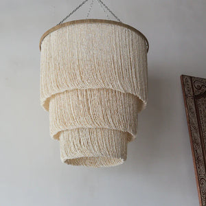 Handmade seashell chandelier with layered design hanging against a neutral wall