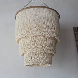 Handcrafted Balinese seashell chandelier with layered cream beaded design, hanging indoors.