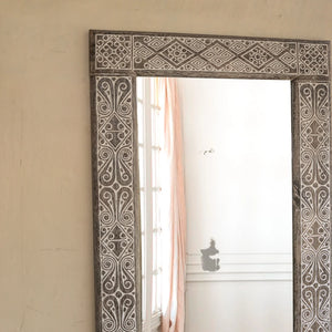 Hand-carved wooden mirror with intricate Balinese patterns in a bright, minimalist room