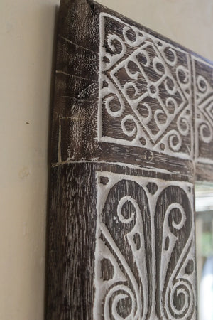 Close-up of hand-carved Balinese wood frame with intricate white swirl patterns
