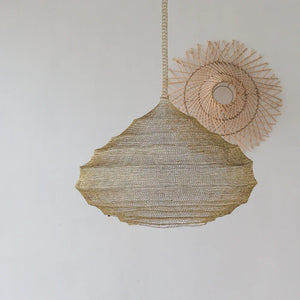 Handwoven natural fiber pendant lamp with a unique organic shape, hanging beside woven wall art