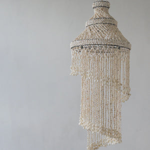 Handmade Balinese seashell chandelier with intricate beadwork against a neutral wall