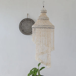 Handmade Balinese seashell chandelier with spiral fringe, boho wall plate, and potted plant