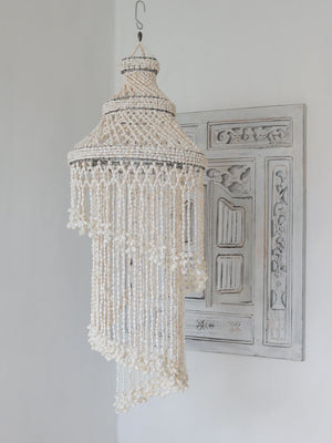 Handcrafted Balinese seashell chandelier with intricate beading, hanging by carved wood decor.