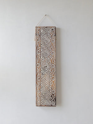 Hand-carved wooden wall art with intricate Balinese geometric patterns on a white wall