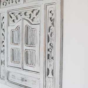Whitewashed hand-carved wooden door with Balinese floral patterns on a white wall