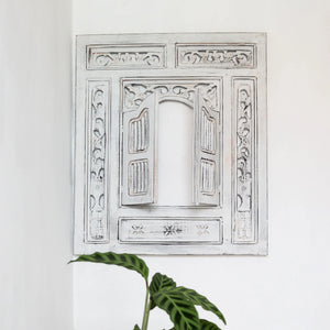 Hand-carved Balinese wall decor with whitewashed wooden window frame and intricate floral details