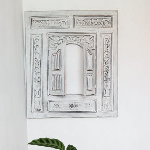 Hand-carved whitewashed wooden Balinese window frame with floral patterns on white wall