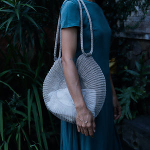 Wire Mesh Hand Woven Bag Ratna held by a person in a blue dress against a lush green background.