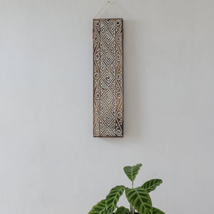 Hand-carved Balinese wooden wall art with geometric patterns above a green plant