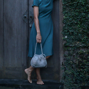 Wire Mesh Hand Woven Bag Lily showcased by a model near a rustic door, emphasizing sustainable fashion.