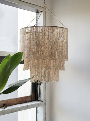 Handmade seashell chandelier with tiered design hanging by a window in a minimalist room