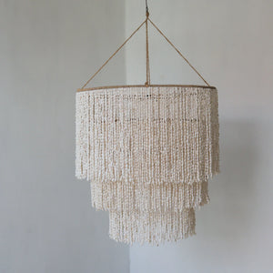 Three-tier seashell chandelier with natural rope, hanging against a plain wall.