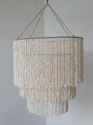 Handmade Balinese seashell chandelier with layered beads, hanging against a plain wall.