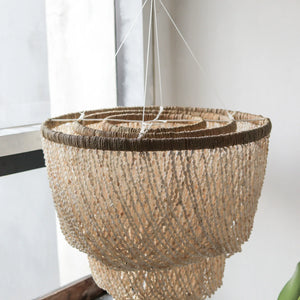 Handmade Balinese seashell chandelier with natural fibers, hanging by a window