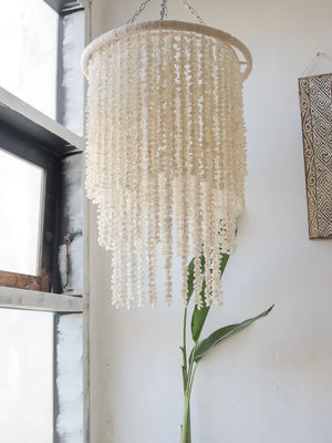 Handmade Balinese seashell chandelier hanging by a window in a bright, minimalist room