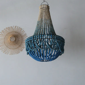 Blue beaded chandelier with natural rattan wall decor on a light grey wall