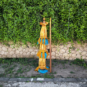 Balinese knock-down parasol with yellow and blue tassels, set against a garden stone wall