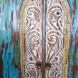 Hand-carved Balinese wooden door with ornate white detailing and rustic blue finish