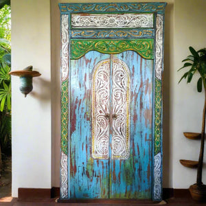 Hand-carved Balinese wooden door with blue, green, and white ornate patterns, tropical decor