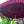 Maroon Balinese umbrella with fringe, decorative patterns, set outdoors with greenery