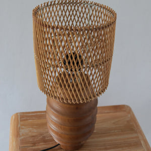 Modern rattan table lamp with wooden base and woven bamboo shade on wood surface