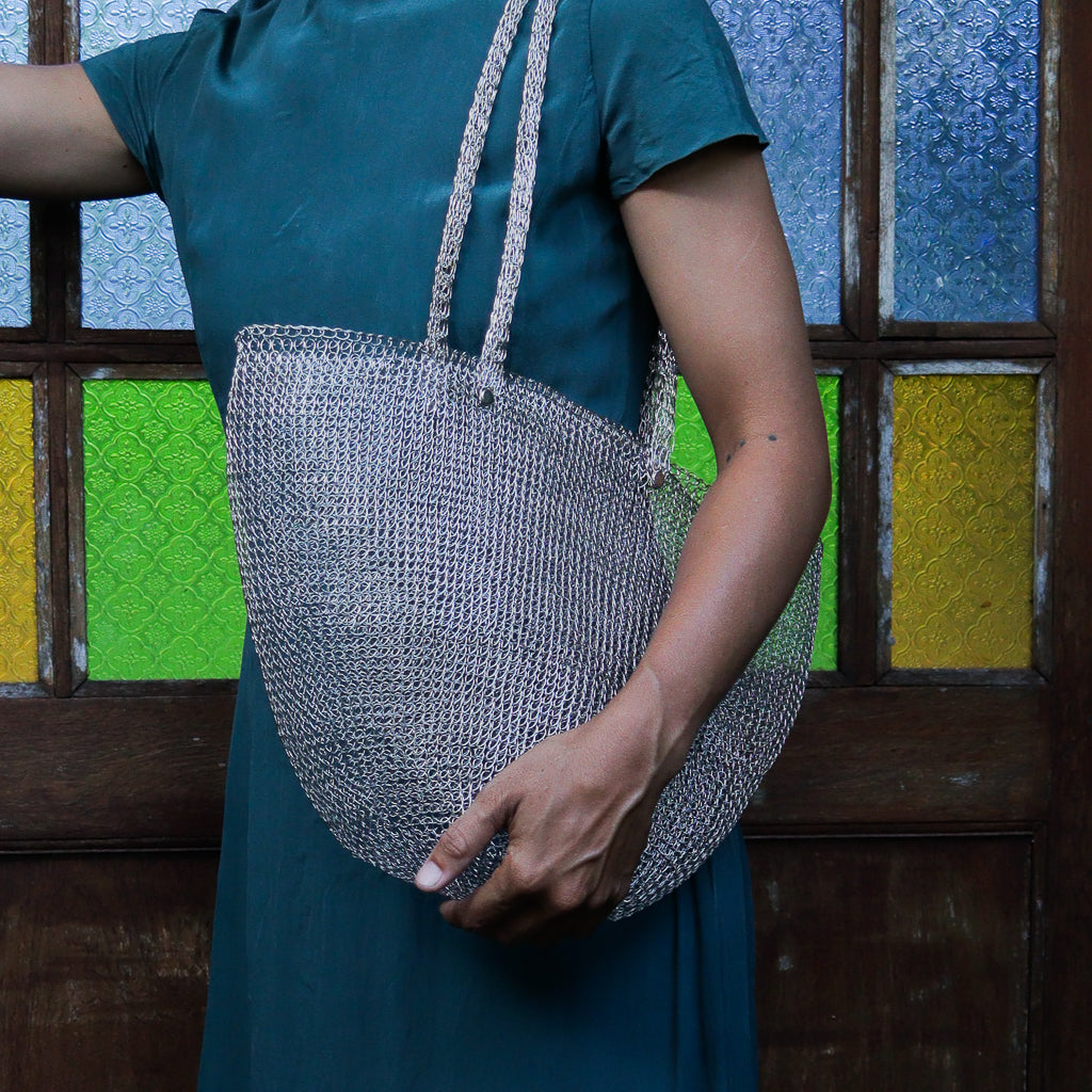 Person holding a textured handbag in front of a colorful stained glass window
