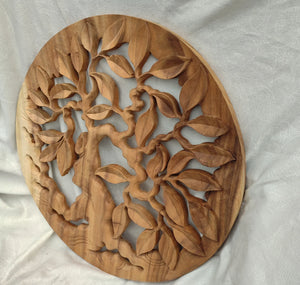 Hand-carved wooden wall art featuring a tree with branches and leaves on a round panel