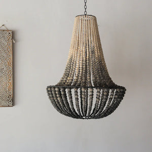 Wooden beaded chandelier hanging against a plain wall with a decorative wall piece.
