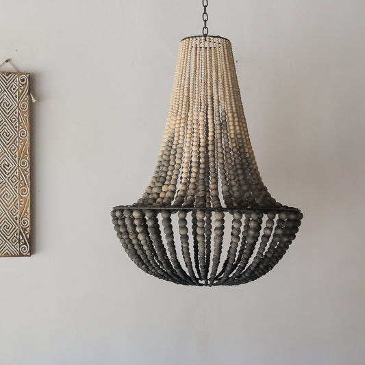 Wooden beaded chandelier hanging against a plain wall with a decorative wall piece.