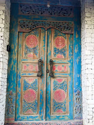 Hand-carved Balinese wooden door with floral patterns and distressed blue paint