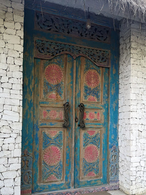Hand-carved Balinese wooden door with floral motifs and colorful distressed finish