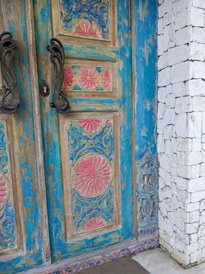 Hand-carved Balinese door with blue and pink floral patterns and ornate handles
