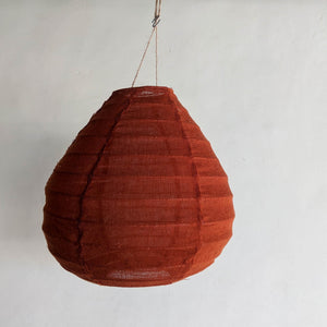 Rustic handwoven rattan pendant light in warm terracotta color against a plain wall