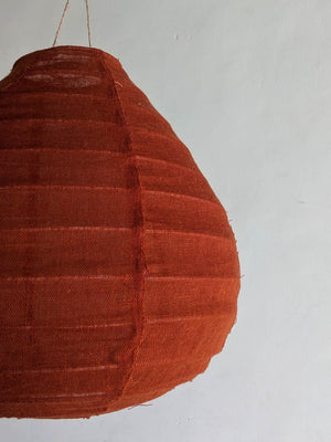 Handmade woven rattan pendant lamp with natural orange fiber, hanging against a neutral wall.