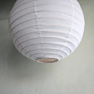 Large round white paper lantern pendant light against a pale green wall.