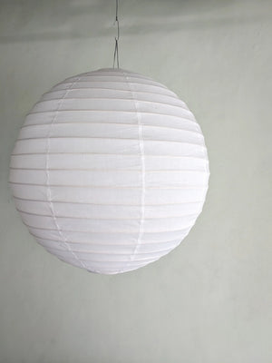 White round paper lantern hanging from ceiling against a plain wall, minimalist home decor