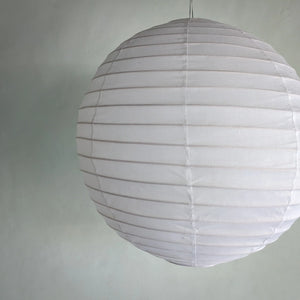 White round paper lantern hanging against a light grey wall, minimal modern decor