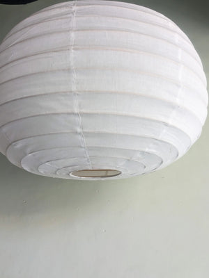 Large white round paper lantern ceiling light against a plain wall, minimalist home decor