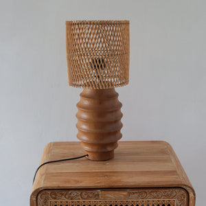 Handcrafted rattan table lamp with woven shade and wooden base on carved furniture