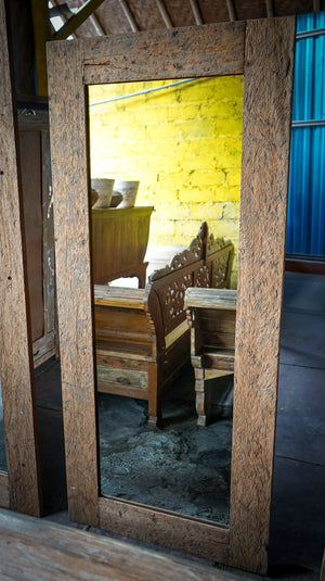 Rustic reclaimed wood frame mirror reflecting carved wooden furniture and textured yellow wall
