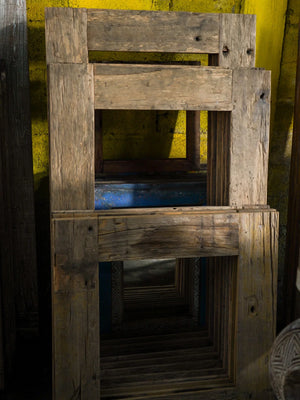 Handmade reclaimed teak wood mirrors with rustic finish stacked against a yellow wall