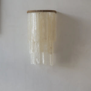 Handmade Balinese capiz shell wall sconce with cascading white shells on neutral wall.