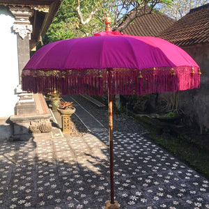 Balinese pink ceremonial umbrella with fringe in a traditional courtyard